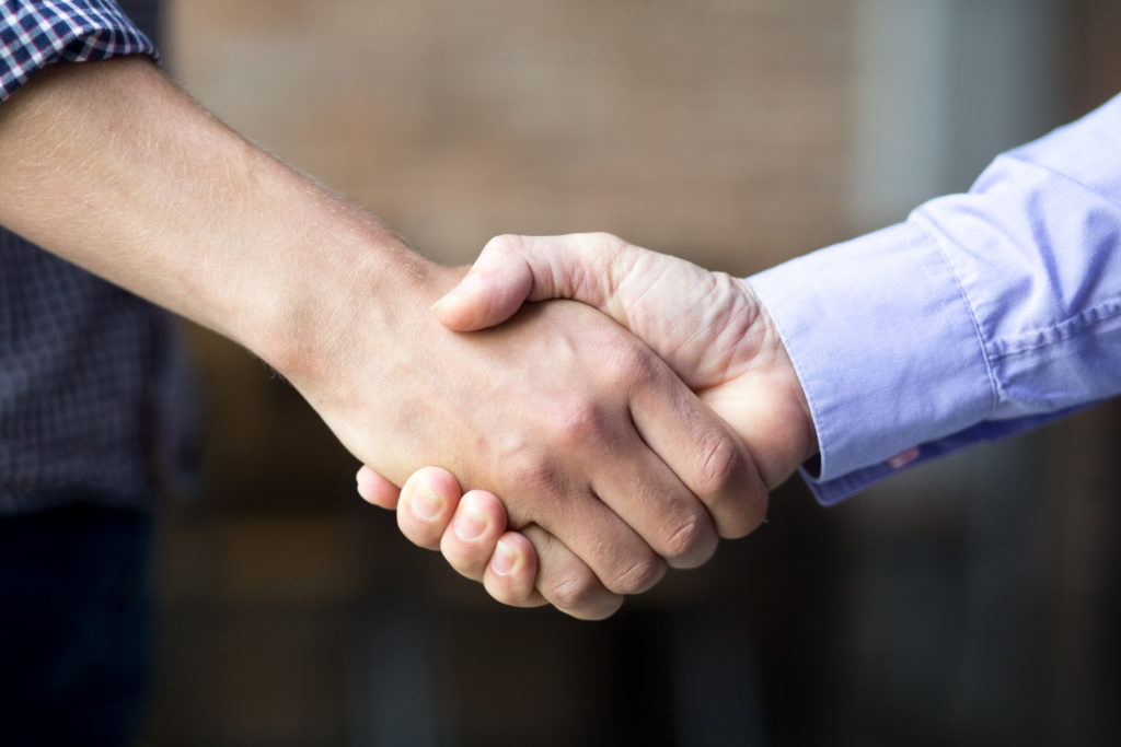 Deux hommes en train de se serrer la main, connotant l'engagement de Clemcom, community manager.